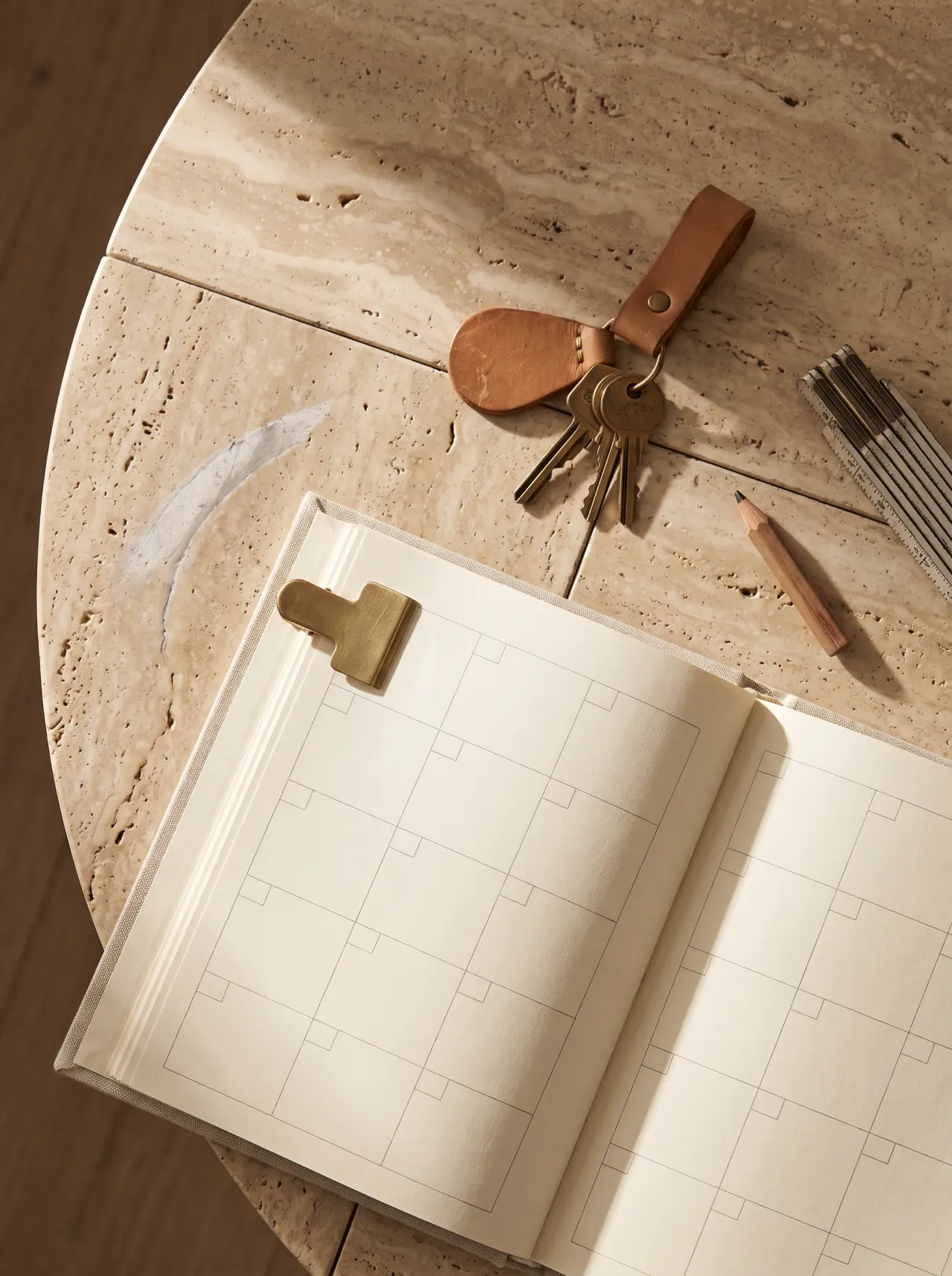 An open desk planner on a travertine top, one date marked with a brass clip, beside keys on a leather fob