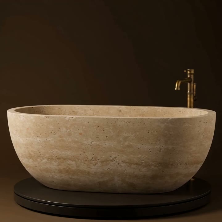 A travertine freestanding bath with an aged brass floor-standing tap on a dark turntable